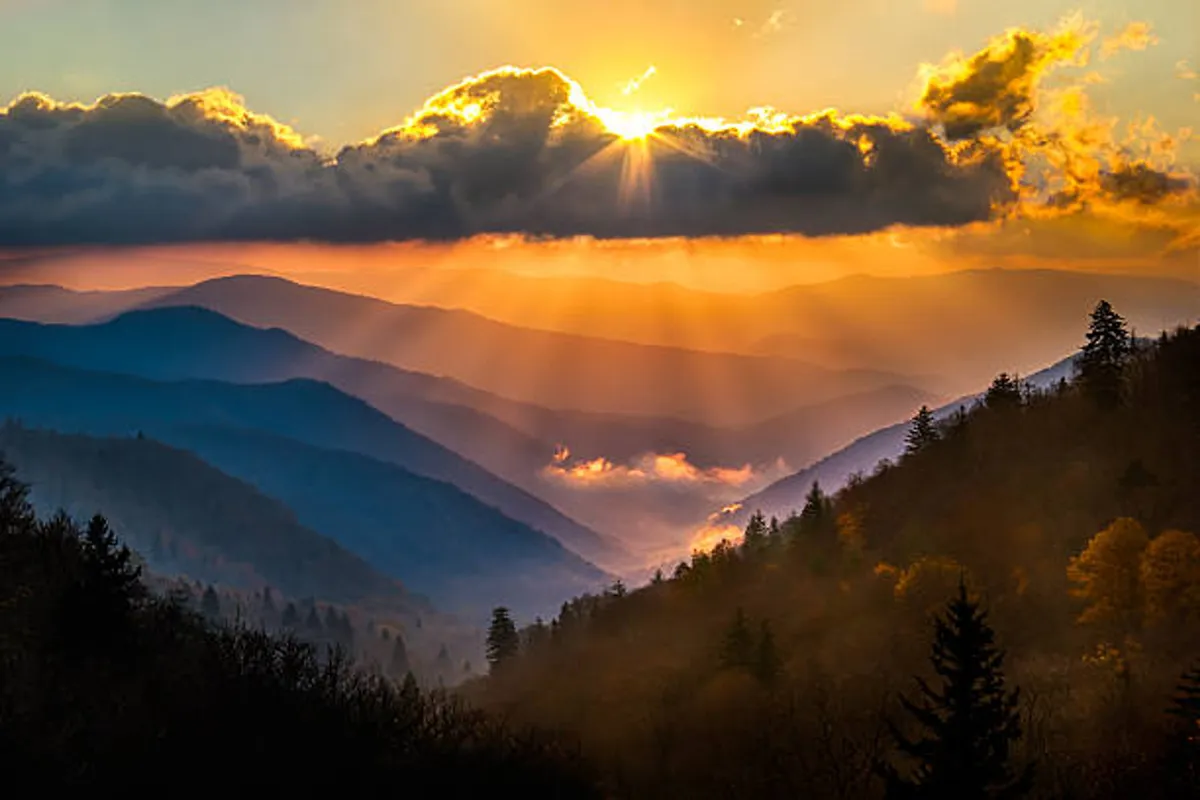 A sweeping view of sunset over mountain ranges, with clouds and soft light painting the scene. The landscape embodies the allure of nearby hiking trails and the natural wonders accessible from the cabin.