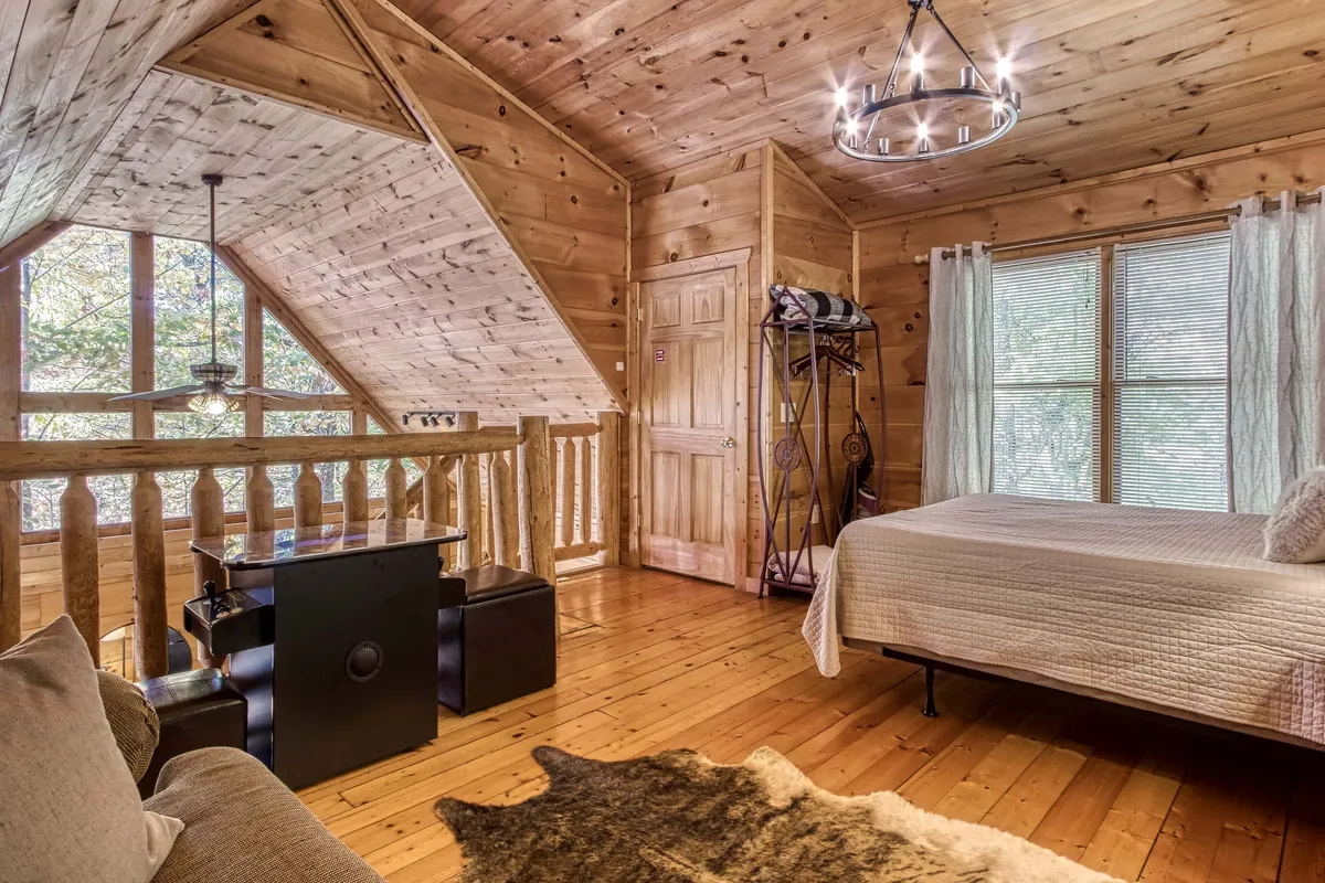 A tranquil bedroom with a wooden ceiling, large windows letting in natural light, a comfortable bed, and a decorative chandelier. The design evokes rustic warmth, while the windows frame views of the outdoors, blending the serenity of indoor comfort with the beauty of the Smokies.