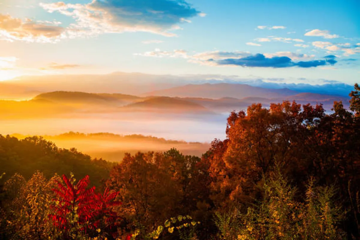 A breathtaking view of the sun setting over misty mountain valleys and forests ablaze with colorful autumn leaves, capturing the region’s natural beauty and tranquil atmosphere.