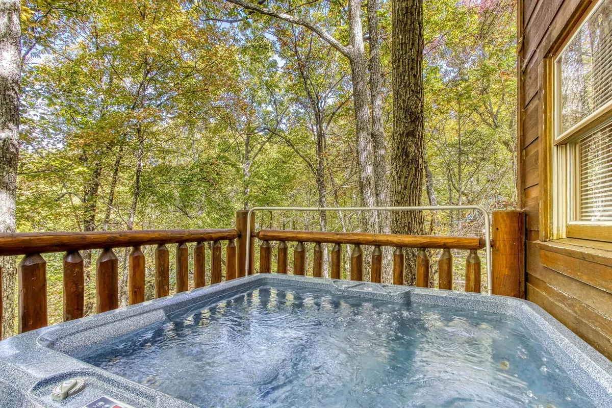 This exterior image centers on a secluded hot tub set against a backdrop of lush trees and a wooden railing, evoking a sense of privacy and tranquility. The space is ideal for relaxing in the warm waters while enjoying nature views or stargazing at night.