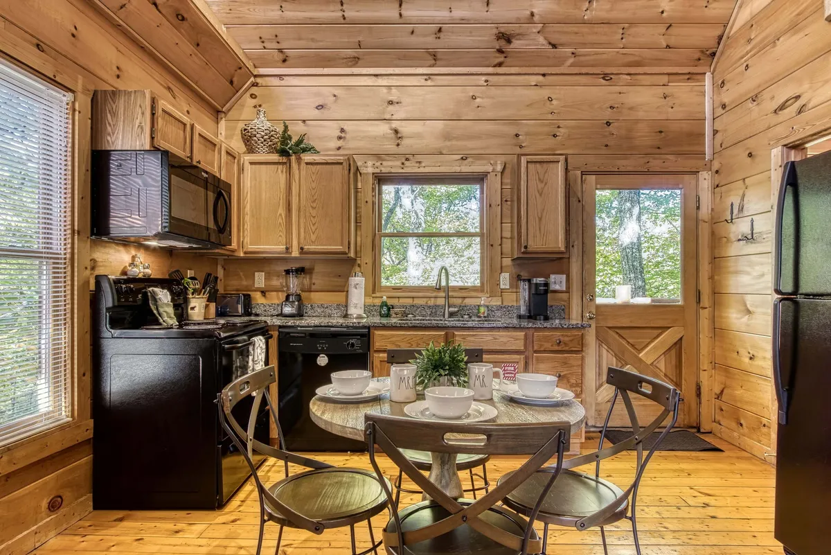 A spacious and elegantly rustic kitchen with natural wood cabinets, a central island, and a large dining table. Bright windows provide ample natural light, making this space perfect for cooking, sharing meals, or morning coffee while enjoying views of the landscape outside.