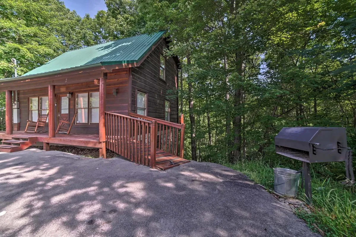 A cozy, tree-framed porch with rocking chairs, a green roof, and an outdoor grill, evoking a rustic mountain retreat. The setting is peaceful and inviting, perfect for enjoying morning coffee or evening relaxation after a day on the trails.