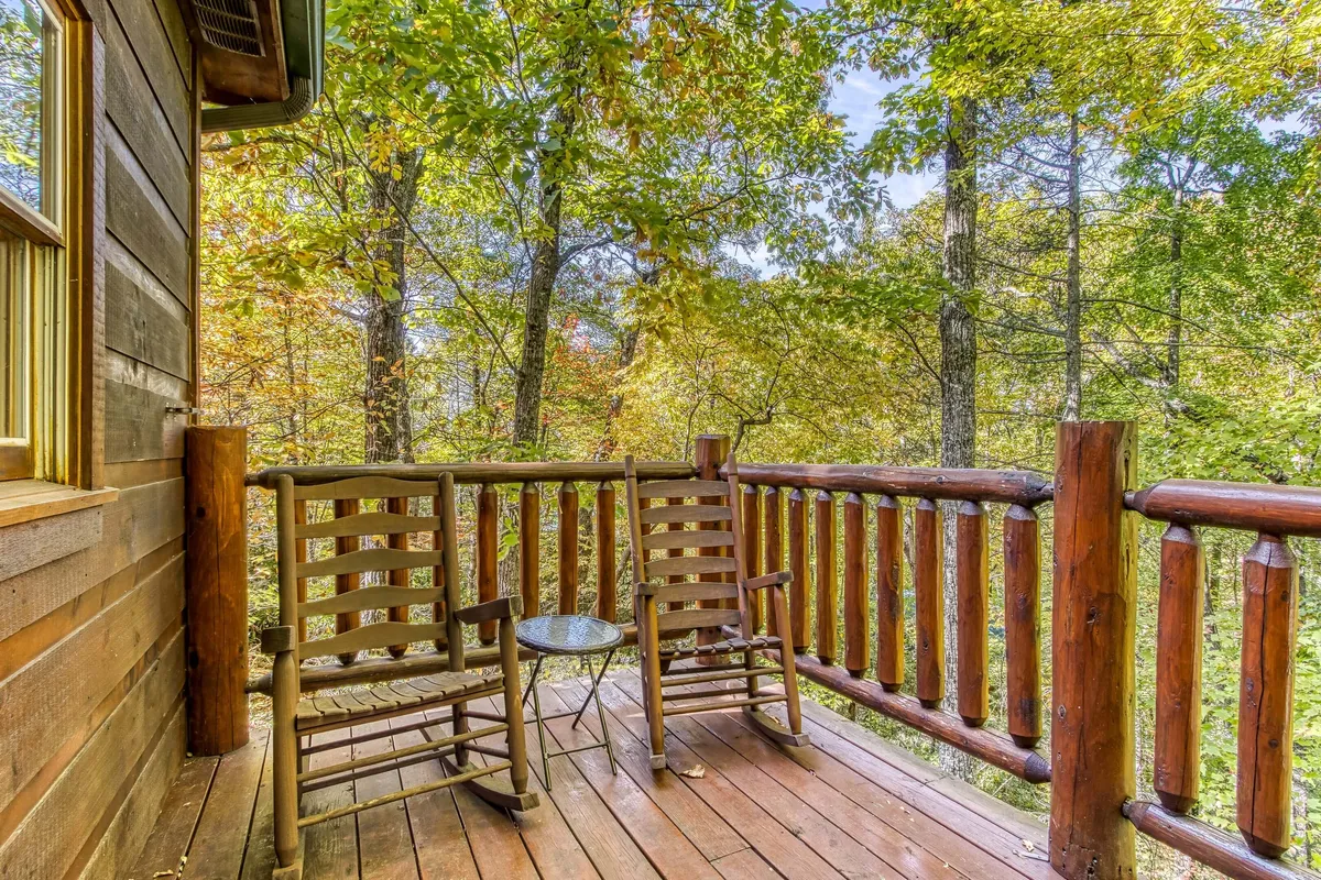 A peaceful wooden deck with classic rocking chairs and a small table, surrounded by tall trees. The secluded setting invites relaxation and provides an ideal spot for unwinding after a hike, with plenty of space for both guests and their pets to enjoy the fresh mountain air.